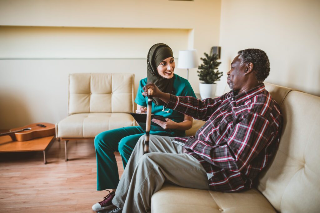 Close-up of smiling senior man with walking stick and friendly nurse. Friendly caregiver talking with a happy elderly man with a walking stick at a sanatorium. A Muslim Female Doctor and her Senior Afro-American Patient