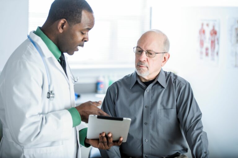 Male doctor explaining something from a clipboard to a male patient.