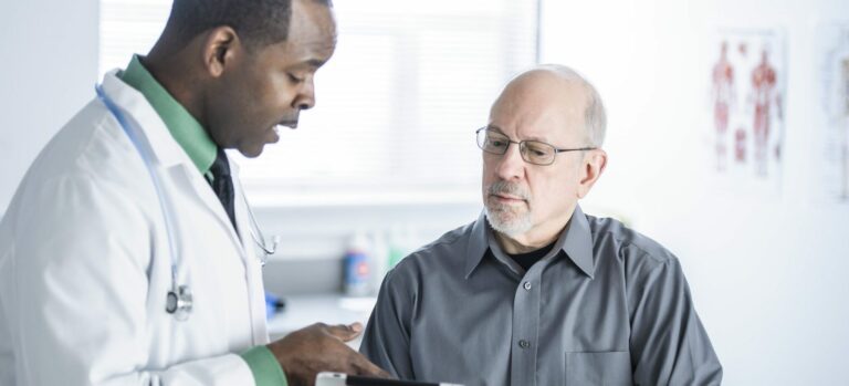 Male doctor explaining something from a clipboard to a male patient.